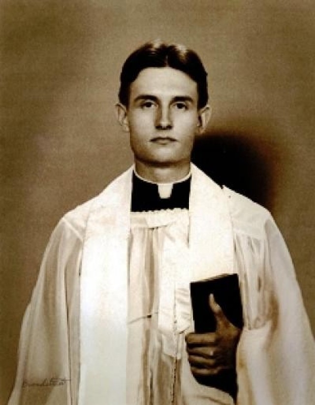 Chaplain (Capt.) Emil J. Kapaun poses for a photo in liturgical dress, holding a bible.