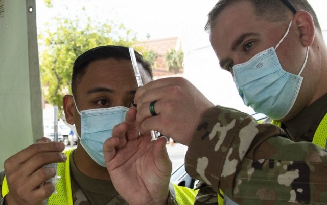 Sgt. Felipe Millan and Spc. Zak Brinkhaus with the 4th Infantry Division, Fort Carson, Colo., inspect vaccine syringes at the California State University Los Angeles Community Vaccination Center, Feb. 15, 2021.