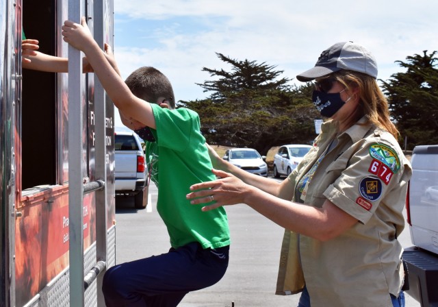 Eugenia Mirfild, right, a Cubmaster with Cub Scout Pack 674 from Santa Cruz, helps a Cub Scout out a window in the Presidio of Monterey Fire Department Fire Safety and Prevention Trailer during the Monterey Cub Scout Camp at the Presidio of Monterey, Calif., July 29.