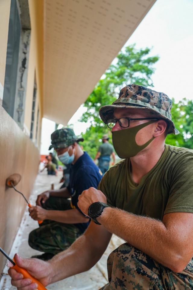 U.S. Marine Corps 2nd Lt. Robert Rogers, Engineering Civic Action Program officer in charge with Bridge Company, 9th Engineer Support Battalion, 3d Marine Logistics Group, and a member of the Royal Thai Mobile Development Unit 12, paint the exterior of the Baan Mai Thai Pattana School, during Exercise Cobra Gold 21, in Sa Kaeo province, Kingdom of Thailand, Aug. 3, 2021. U.S. Marines joined Royal Thai Armed Forces to construct an 8 X 20-meter multipurpose facility that will help accommodate the school’s growing number of students, enable educational opportunities and community development, and continue to strengthen bonds between the U.S. and Thai armed forces. Cobra Gold 21 emphasizes security cooperation as well as civic actions, such as humanitarian assistance and disaster relief, and seeks to expand regional cooperation among like minded allies and partners. (U.S. Marine Corps photo by Cpl. Moises Rodriguez)
