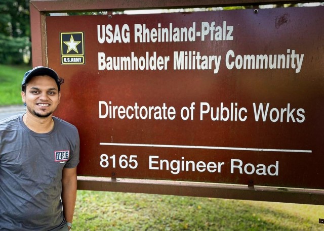 Paras Upreti stands in front of the sign for the Directorate of Public Works in the Baumholder Military Community, Germany, Aug. 24. Upreti, an employee of U.S. Army Garrison Rheinland-Pfalz, is volunteering Urdu language simultaneous interpretation services as thousands of Afghan evacuees stream into the Kaiserslautern Military Community and stay on Ramstein Air Base and the garrison's Rhine Ordnance Barracks site.