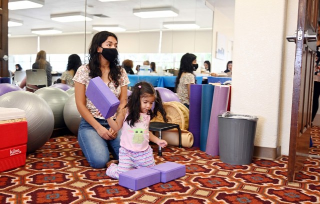Marlen Lucero, a military spouse, listens during the Presidio of Monterey Military Spouse Orientation at the General Stilwell Community Center, Ord Military Community, Calif., Aug. 23, as her daughter, Scarlet, 2, plays.