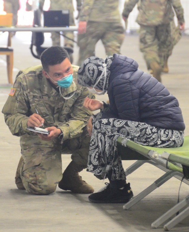 Staff Sgt. Roberto Molina, a Landstuhl Regional Medical Center respiratory technician, takes information from one of the evacuees. (Photo Credit: Shaylee Rawls Borcsani)