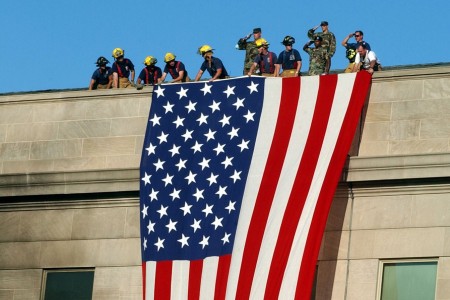 Military service members salute while fire and rescue workers unfurl a massive American flag over the side of the Pentagon on Sept. 12, 2001, as rescue and recovery operations continued following the 9/11 terrorist attack.  They include Sgt. William K. Wilkins, wearing a beret, standing third from the right. The Ordnance Corps Soldier and his mobile communications crew were among the initial wave of those responding to the scene.  Wilkins is a now a chief warrant officer 4 assigned to U.S. Army Combined Arms Support Command headquartered at Fort Lee, Va. 