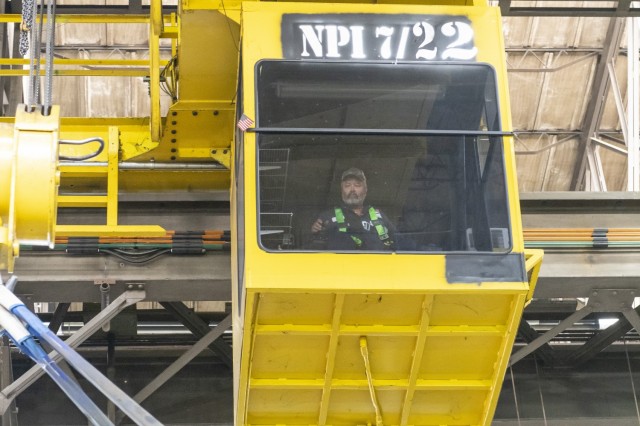 In the Combat Vehicle Repair Facility, David Ivey, a high level crane operator, focuses on the M1 hull and the ground guides providing assistance.