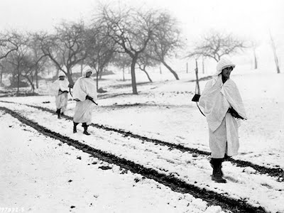 Three members, of an American patrol, Sgt. James Storey, of Newman, Ga., Pvt. Frank A. Fox, of Wilmington, Del., and Cpl. Dennis Lavanoha, of Harrisville, N.Y., cross a snow-covered Luxembourg field on a scouting mission in Lellig, Luxembourg, Dec. 30, 1944. White bedsheets camouflage them in the snow.